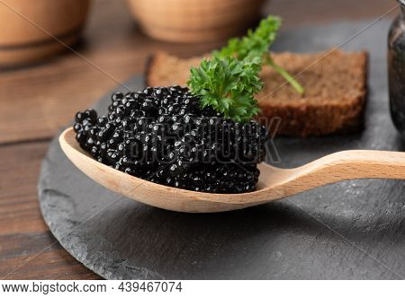 Fresh Grainy Black Paddlefish Caviar In Brown Wooden Spoon On A Black Background, Close Up