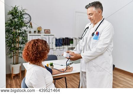 Middle age man and woman wearing doctor uniform using tensiometer having medical consultation at clinic