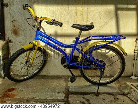 Stock Photo Of Blue And Yellow Color Bicycle Parked Outside Of The House Near Wall Under Bright Sunl