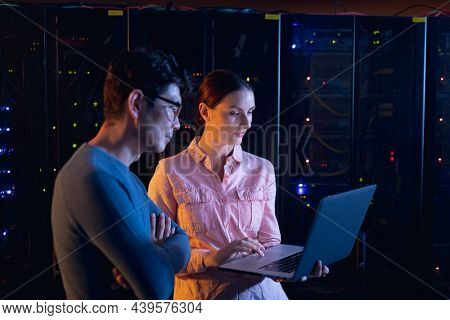 Diverse male and female engineers using laptop in computer server room. database server management and maintenance concept