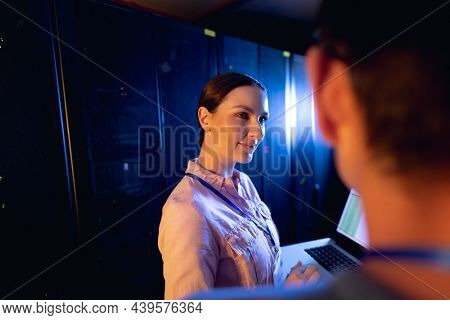Caucasian female engineer using laptop in computer server room. database server management and maintenance concept