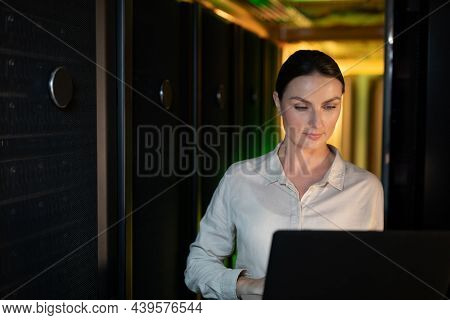 Caucasian female engineer using laptop in computer server room. database server management and maintenance concept