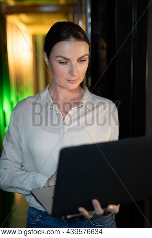 Caucasian female engineer using laptop in computer server room. database server management and maintenance concept