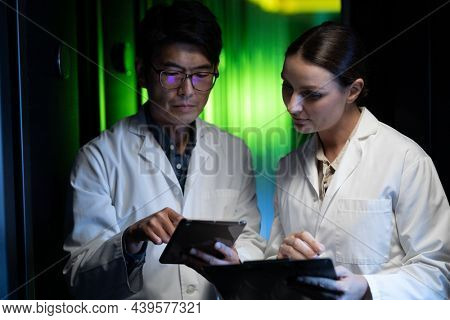 Diverse male and female engineers wearing aprons using digital tablet in computer server room. database server management and maintenance concept