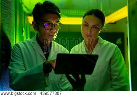 Diverse male and female engineers wearing aprons using digital tablet in computer server room. database server management and maintenance concept