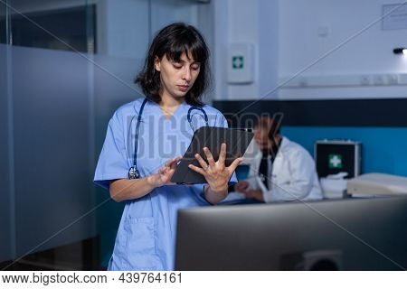 Woman Nurse Looking At Digital Tablet Working Late At Night. Medical Assistant Holding Modern Gagdet