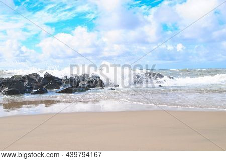Ocean Waves Breaking On Stones And Rocks Near Sandy Beach. Splashing Salty Water Forming Foam Near E