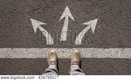 Arrows Drawn On The Asphalt In Different Directions In Front Of Your Feet In Boots. View From Above.