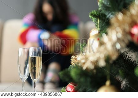 Close-up Of Two Glasses Near Decorated Christmas Tree And Sad Woman Sitting Alone. Broke Up With Gir