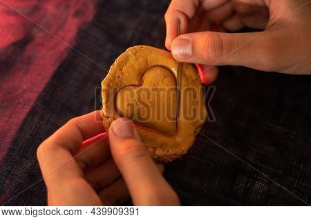 Hands closeup scratch brown sugar caramel candy cookies with a metal needle in the shape of a heart on a white backgound