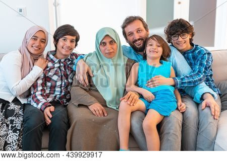Portrait photo of an arab muslim family sitting on a couch in the living room of a large modern house. Selective focus 