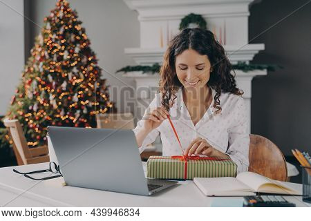 Young Happy Excited European Woman Office Worker Untying Bow On Xmas Gift Box While Sitting At Her W