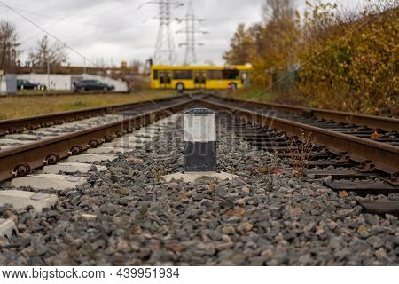 Photo Of Railway Tracks Connected At One Distant Point. Bus In The Background. Railroad Pole Marker.