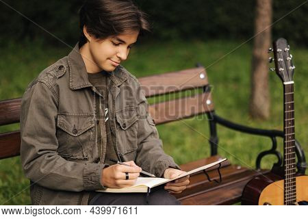 Talanted Person Is Talanted In Everything. Teenager Writes Lyrics For A Song. Boy Using Acoustic Gui