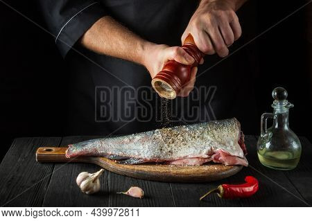 Chef Prepares Fresh Fish Sprinkling Pepper. Preparing To Cook Fish Food. Working Environment In The 