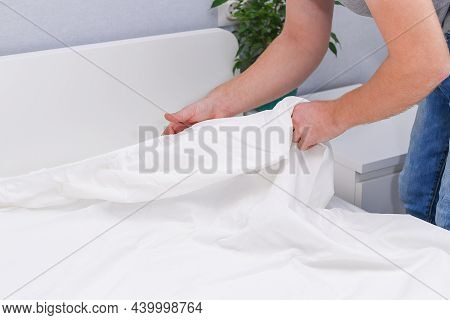 A Man Puts An Elasticated Sheet On The Mattress. Change Of Bed Linen.