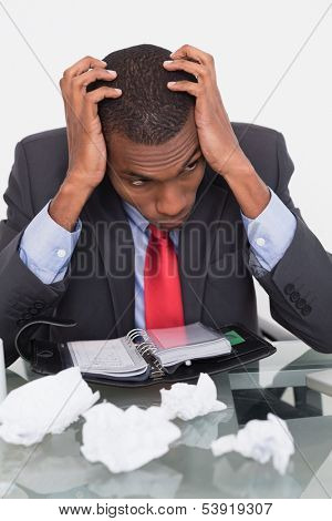 Frustrated young Afro businessman with head in hands at desk against white background