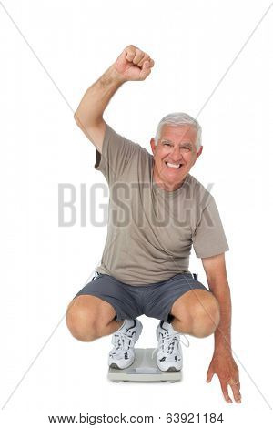 Full length portrait of a senior man cheering on weight scale over white background