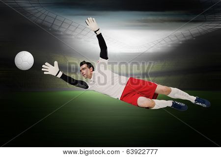 Goalkeeper in white making a save in a large football stadium with lights