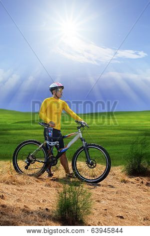 Young Man Standing Beside Moutain Bike  On Hill With Sun Shining On Blue Sky
