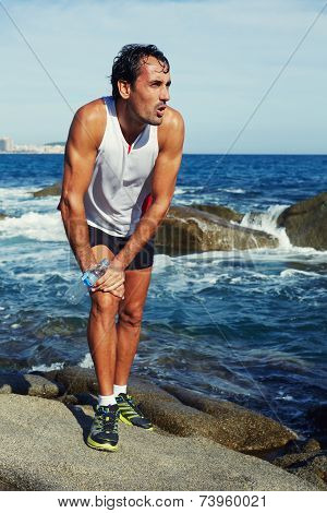 Tired athlete in bright sportswear taking break on beach