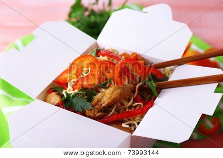 Chinese noodles and sticks in takeaway box on green napkin on pink background