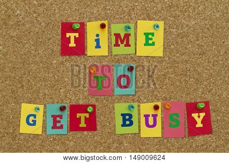 TIME TO GET BUSY message written on colorful sticky notes pinned on cork board.