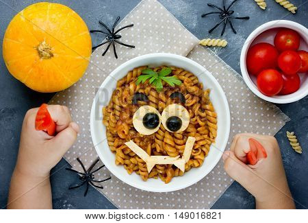 Child eat pasta with sauce in the shape of a smiling vampire face funny dinner or lunch in Halloween style. Creative idea for schoolboy food. Fun with food consept top view