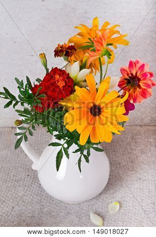 Bouquet from yellow and orange colors in a white vase. Marygold gerberas and dahlias in a white ceramic jug on a gray background