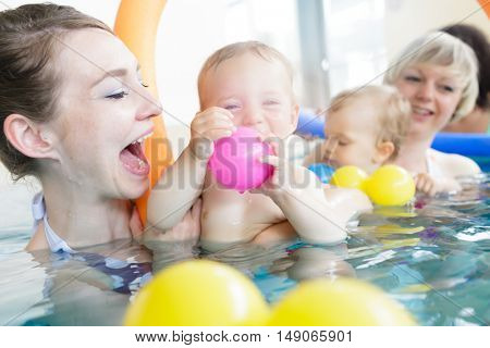 Mothers and their kids having fun at baby swimming lesson between lots of water balls