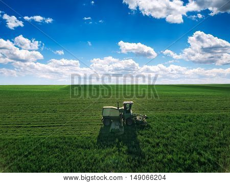 Tractor mowing green field and bkue sky with clouds