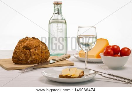 Healthy summer lunch spread out on a tale with a crusty loaf of bread sandwich cheese and bowl of ripe red tomatoes accompanied by fresh water to drink