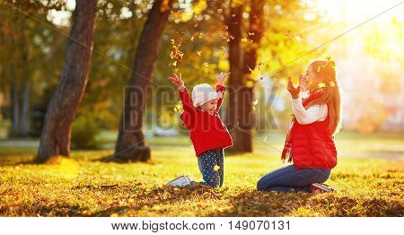 happy family mother and child girl playing and throw leaves in autumn park outdoors