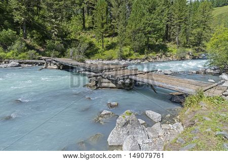 Old wooden bridge at the end of the Kucherla lake whence the river Kucherla follows. Altai Mountains Russia. Sunny summer day.