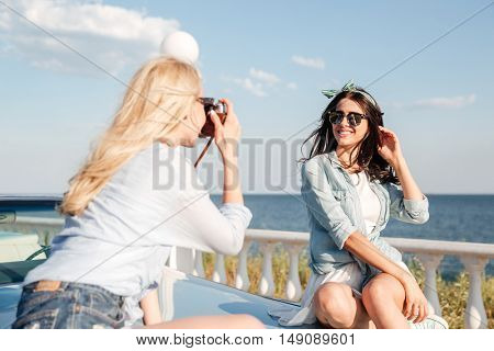 Cheerful attractive young woman sitting and posing to girl photographer in summer