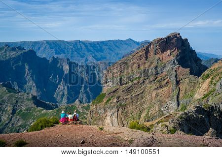Group of tourists is sitting on the cliff. Pico Arieiro to Pico Ruivo hiking route. Madeira island, Portugal.