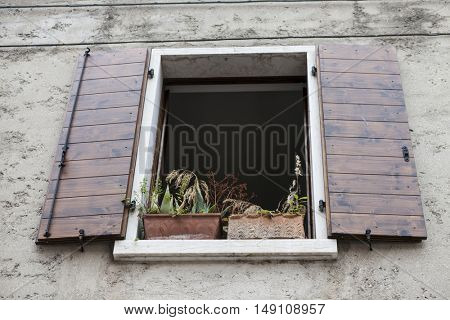Old window with open shutters with flowers on the window sill on the stone wall. Italian Village.