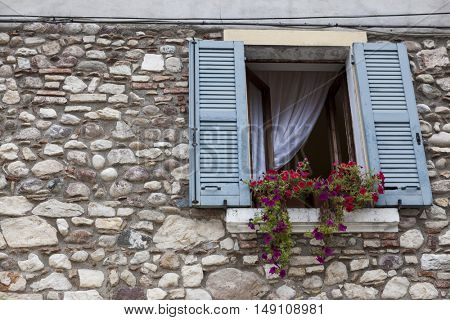 Old window with open shutters with flowers on the window sill on the stone wall. Italian Village.