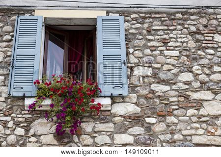 Old window with open shutters with flowers on the window sill on the stone wall. Italian Village.