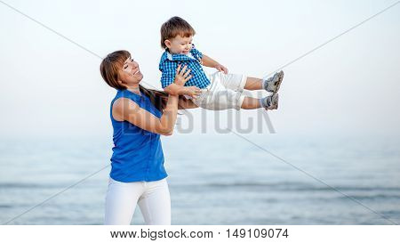 Woman toss the boy up. Behind Ocean and clean sandy beach