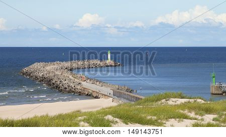Seascape with a lone lighthouse and a concrete breakwater in the foreground against blue sky. Ventspils Latvia