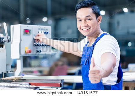 Worker showing thumbs up in Asian production plant standing in front of a machine control board