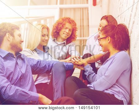 business, office, gesture and startup concept - smiling creative team with hands on top of each other sitting on staircase