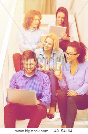 business, technology and startup concept - smiling creative team with laptop and tablet pc computer sitting on staircase