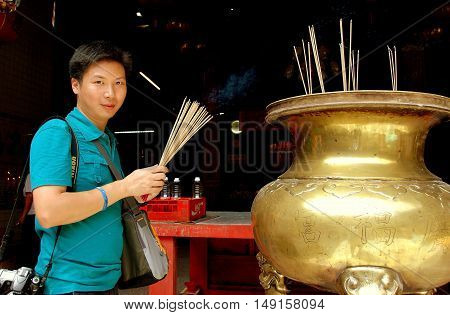 Georgetown Malaysia - January 7 2008: Asian man holding wooden incense sticks standing next to a bronze brazier at the 1801 Guan Yin Chinese temple