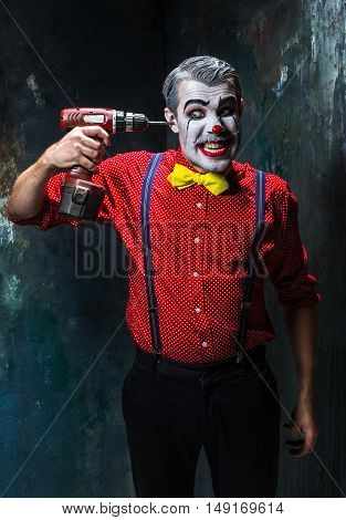 The scary clown and electric drill on dack. Halloween concept of horror and murderer