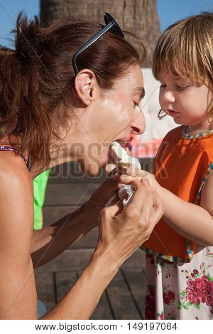 woman eating enjoying white popsicle ice cream from three years old blonde child hands with orange bib in exterior