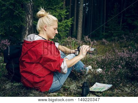 Young active woman tourist drinking tea from a thermos and sitting in the forest. Tourism. Healthy active lifestyle concept
