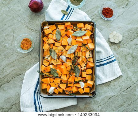 Chopped orange butternut squash on baking sheet with herbs/Diced Squash