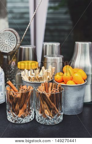 Making mulled wine for sale at country fair. Glintwine accesories, stirring wooden sticks, spices and citrus, cinnamon sticks and kumquat in glasses and metal bowls closeup. Vertical image